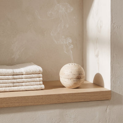 The Stone Burner on a narrow bathroom shelf beside folded towels