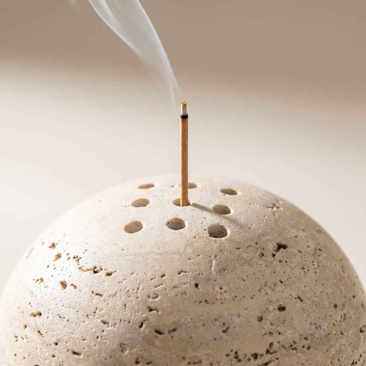An incense stick standing in one of the drilled holes, smoke rising